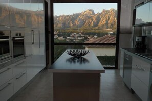 A modern kitchen with a large window offering a view of a mountainous landscape and a village below.