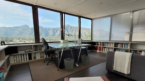 A modern office with a desk, chair, and bookshelf, overlooking a mountainous landscape.