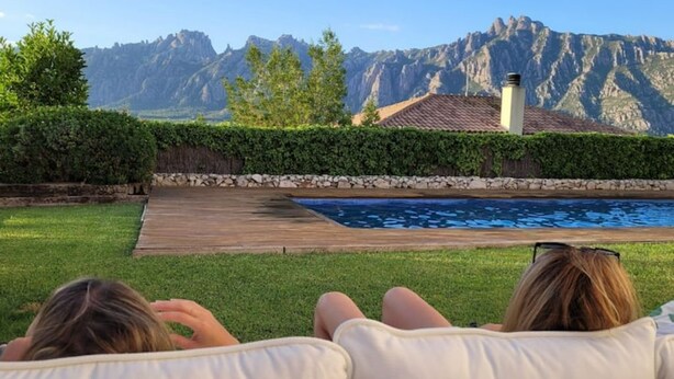 A poolside view with a mountain backdrop, a wooden deck, and a hedge.