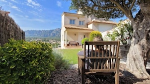 A wooden bench in a garden with a view of a house and mountains in the background.