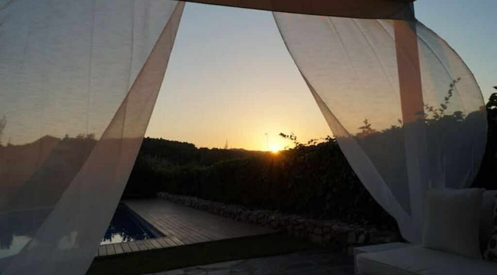 Un belvédère offrant une vue sur le coucher de soleil, avec une piscine et un jardin en contrebas.