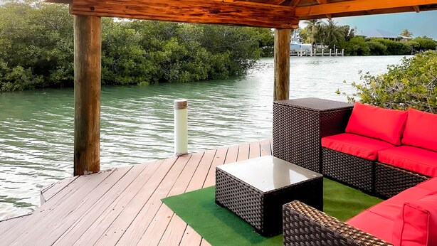 Een houten terras met rieten meubels en een glazen tafel, met uitzicht op een wateroppervlak waar een boot afgemeerd ligt.