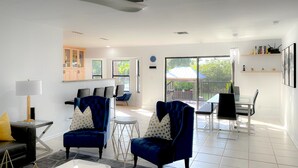 Een moderne woonkamer met twee blauwe fauteuils, een witte salontafel en een glazen eettafel.