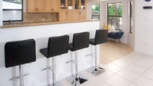 Een moderne keuken met houten kastjes, een granieten aanrechtblad en vier zwarte barstoelen.