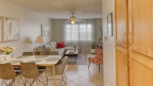 A living room with a dining table, sofa, and chairs. There is a ceiling fan, a window with curtains, and a door. - Beautiful Condo in Dunedin. 5 min from the beach! (Dunedin)
