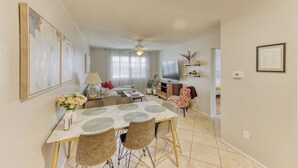 A living room with a sofa, TV, and a dining area with a table and chairs. - Beautiful Condo in Dunedin. 5 min from the beach! (Dunedin)
