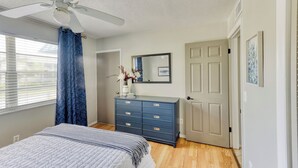 A bedroom with a bed, a dresser, a ceiling fan, a door, and a window with curtains. - Beautiful Condo in Dunedin. 5 min from the beach! (Dunedin)