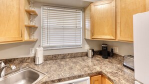 A kitchen with granite countertops, wooden cabinets, a stainless steel sink, a kettle, a coffee maker, and a toaster. - Beautiful Condo in Dunedin. 5 min from the beach! (Dunedin)