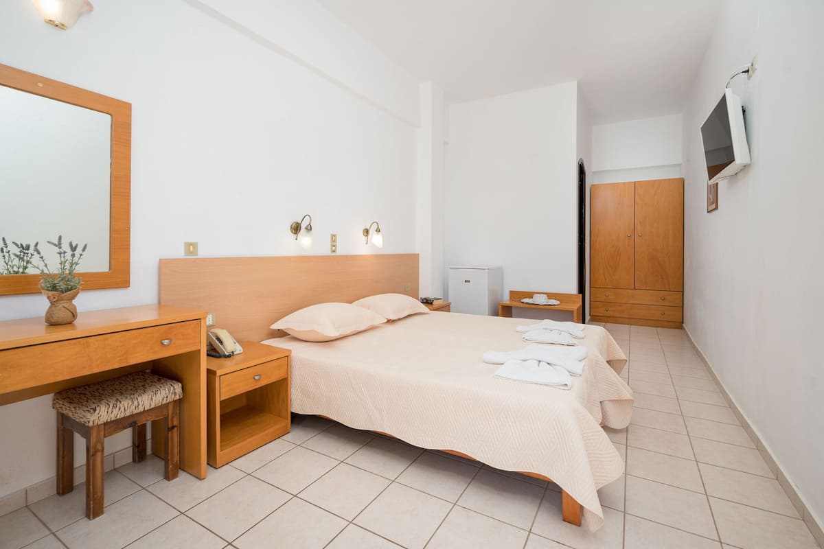 Un dormitorio ordenado con cama, mesita de noche, lámpara y espejo.