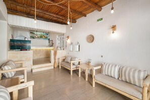 A room with a wooden ceiling, a stone fireplace, a sofa, and a television. - Adonis Hotel (Agios Vasileios)