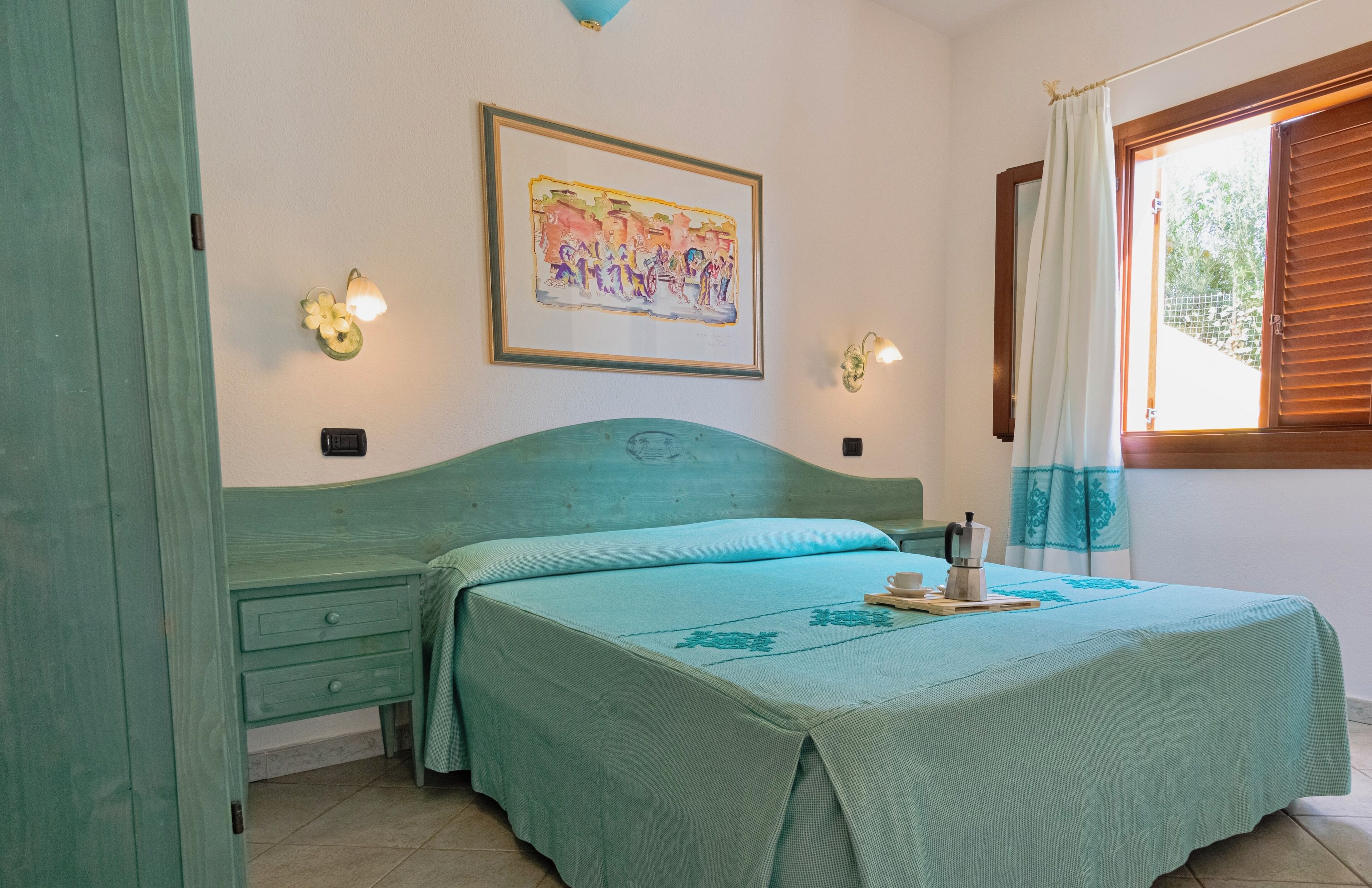Une chambre à coucher avec une couvre-lit turquoise, un tableau encadré au mur et une fenêtre avec des rideaux.