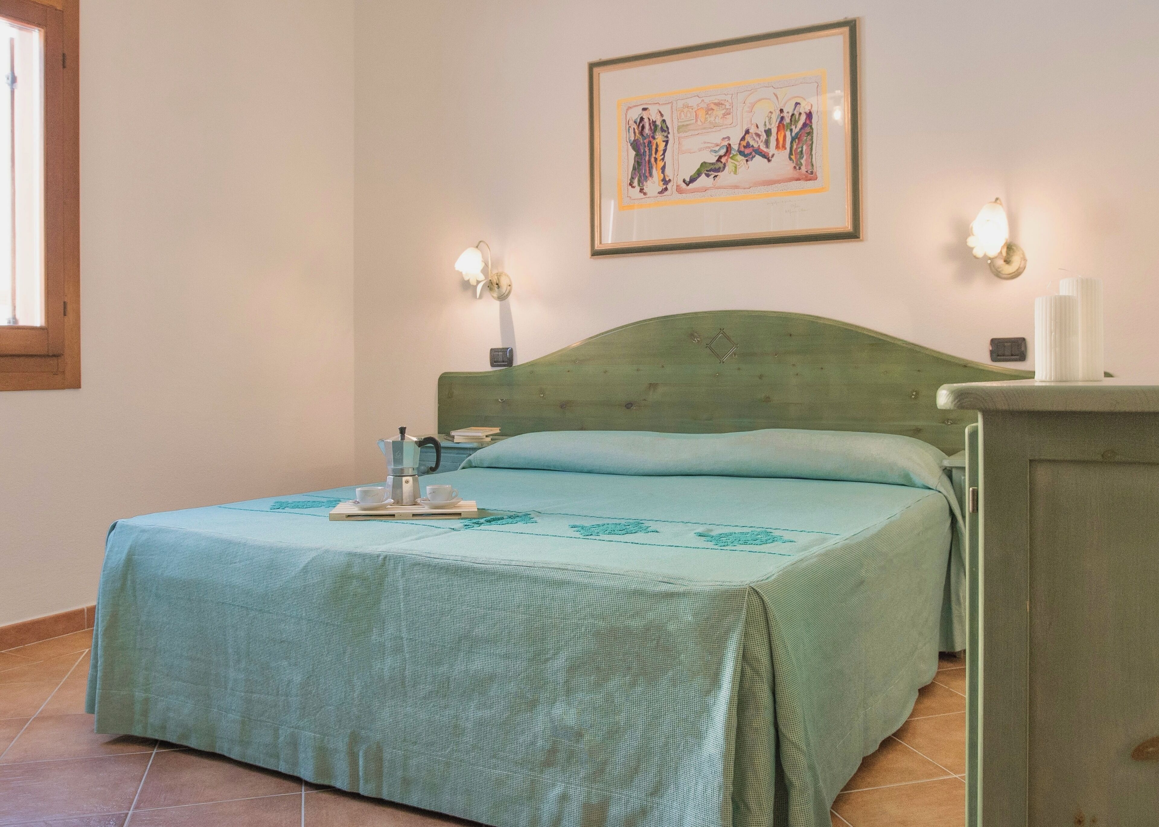 A neatly made bed with a green bedspread, a bedside table with a lamp, and a framed picture on the wall.