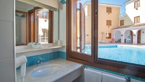 Un baño con un lavamanos amplio, un espejo y vista a una piscina.