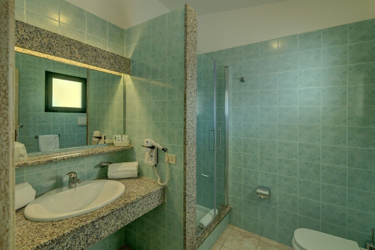 Un baño con lavamanos de encimera de granito, un espejo, cabina de ducha de cristal y un inodoro.