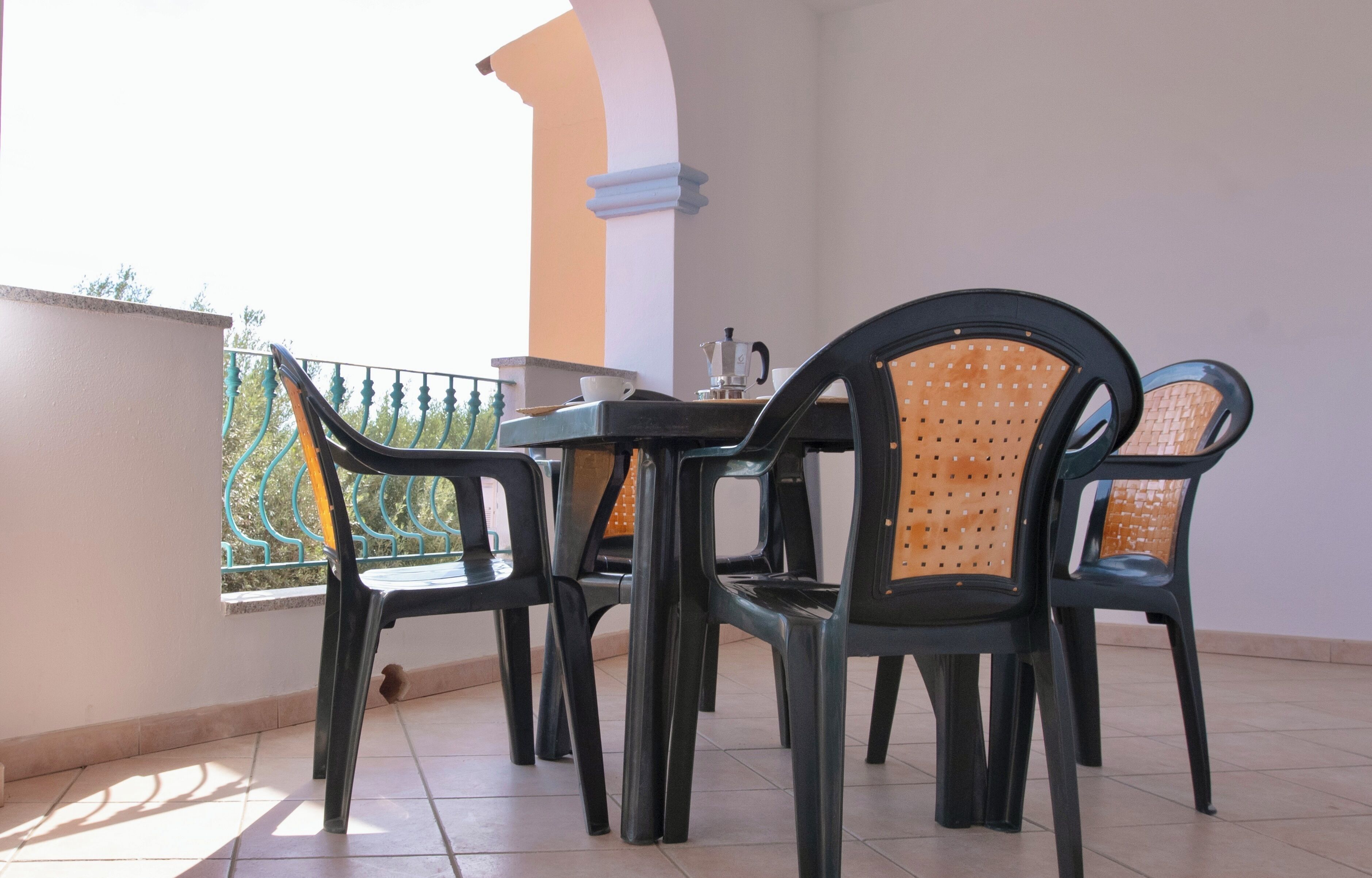 Ein Balkon mit Tisch und Stühlen, einer Kaffeemaschine und Blick auf einen grünen Zaun.