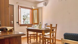 Un comedor con una mesa y sillas de madera, una ventana con vista a árboles y un equipo de aire acondicionado en la pared.