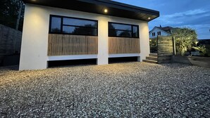 A modern building with two large windows and a sloped roof, surrounded by gravel. - Maygrove Retreat - Sleeps 2 - Jacuzzi & Boat Hire (Staines)