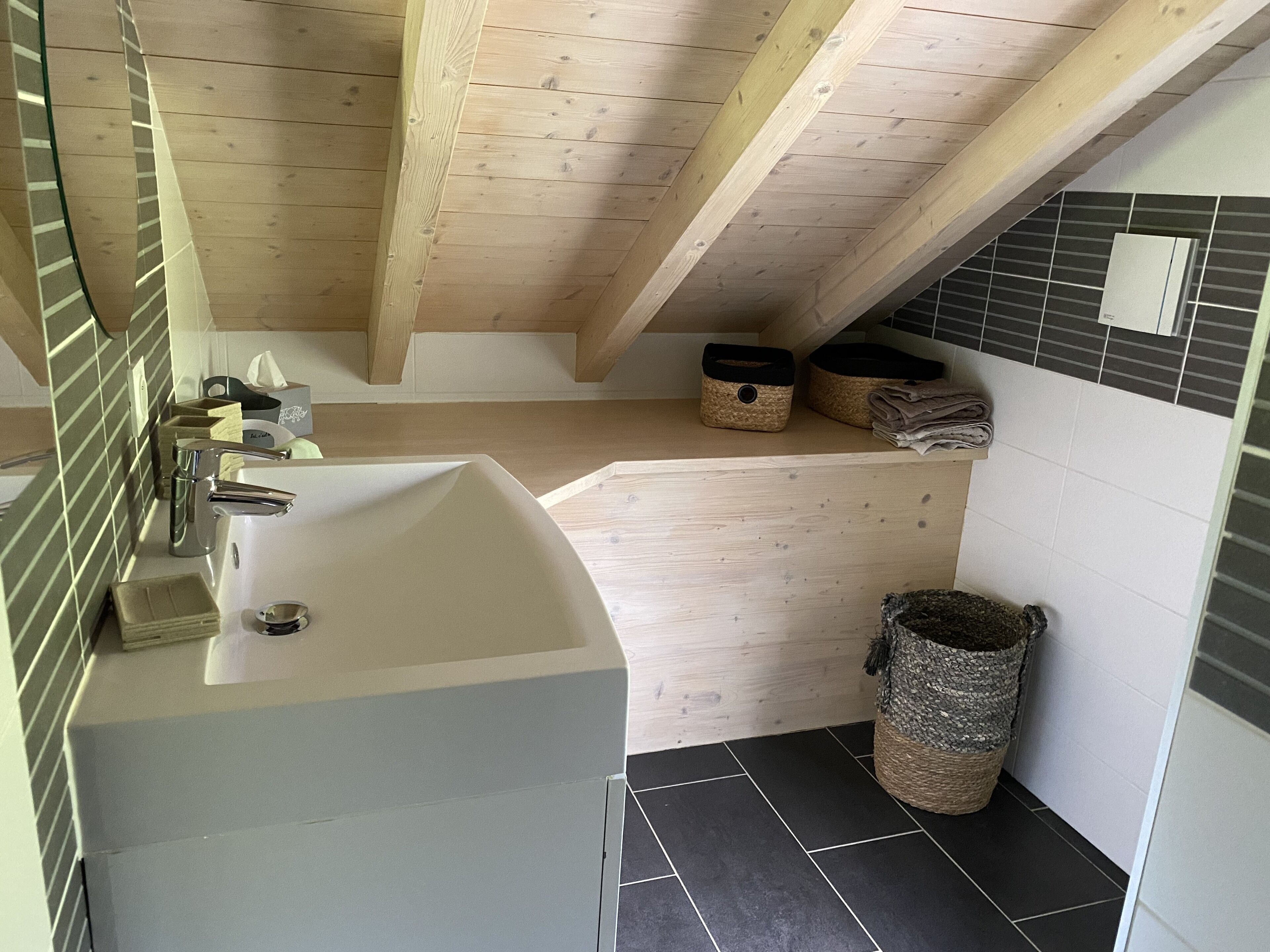 A bathroom with a white sink, wooden ceiling beams, a tiled shower area, and two woven baskets on the shelf.