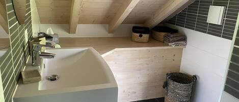 A bathroom with a white sink, wooden ceiling beams, a tiled shower area, and two woven baskets on the shelf.
