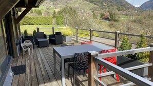 A wooden deck with outdoor furniture, a view of a mountainous landscape, and a small building in the background. - CHARMING, COSY DUPLEX CHALET BETWEEN LAKE AND MOUNTAINS (Dingy-Saint-Clair)