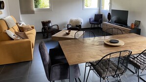 A modern living room with a sofa, dining table, chairs, a TV, and a fireplace. - CHARMING, COSY DUPLEX CHALET BETWEEN LAKE AND MOUNTAINS (Dingy-Saint-Clair)