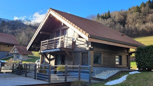 A modern two-story house with a wooden deck and a balcony, surrounded by a grassy yard and a hilly landscape. - CHARMING, COSY DUPLEX CHALET BETWEEN LAKE AND MOUNTAINS (Dingy-Saint-Clair)