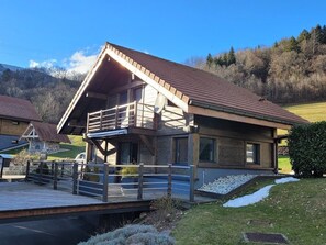 A modern two-story house with a wooden deck and a balcony, surrounded by a grassy yard and a hilly landscape. - CHARMING, COSY DUPLEX CHALET BETWEEN LAKE AND MOUNTAINS (Dingy-Saint-Clair)