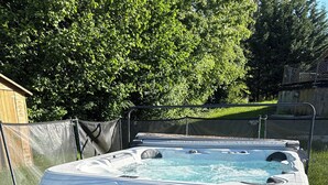A hot tub with a wooden exterior, a step for access, and a metal fence in the background. - Enchanted cabin with shared pool/SPA and optional Kota grill (Loray)