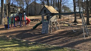 Un parque infantil con tobogán, columpios y una pequeña casita de madera.