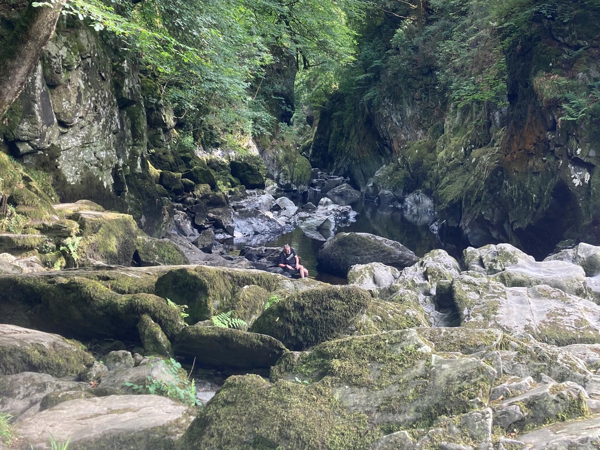 A natural rocky landscape with a person sitting on a moss-covered rock.