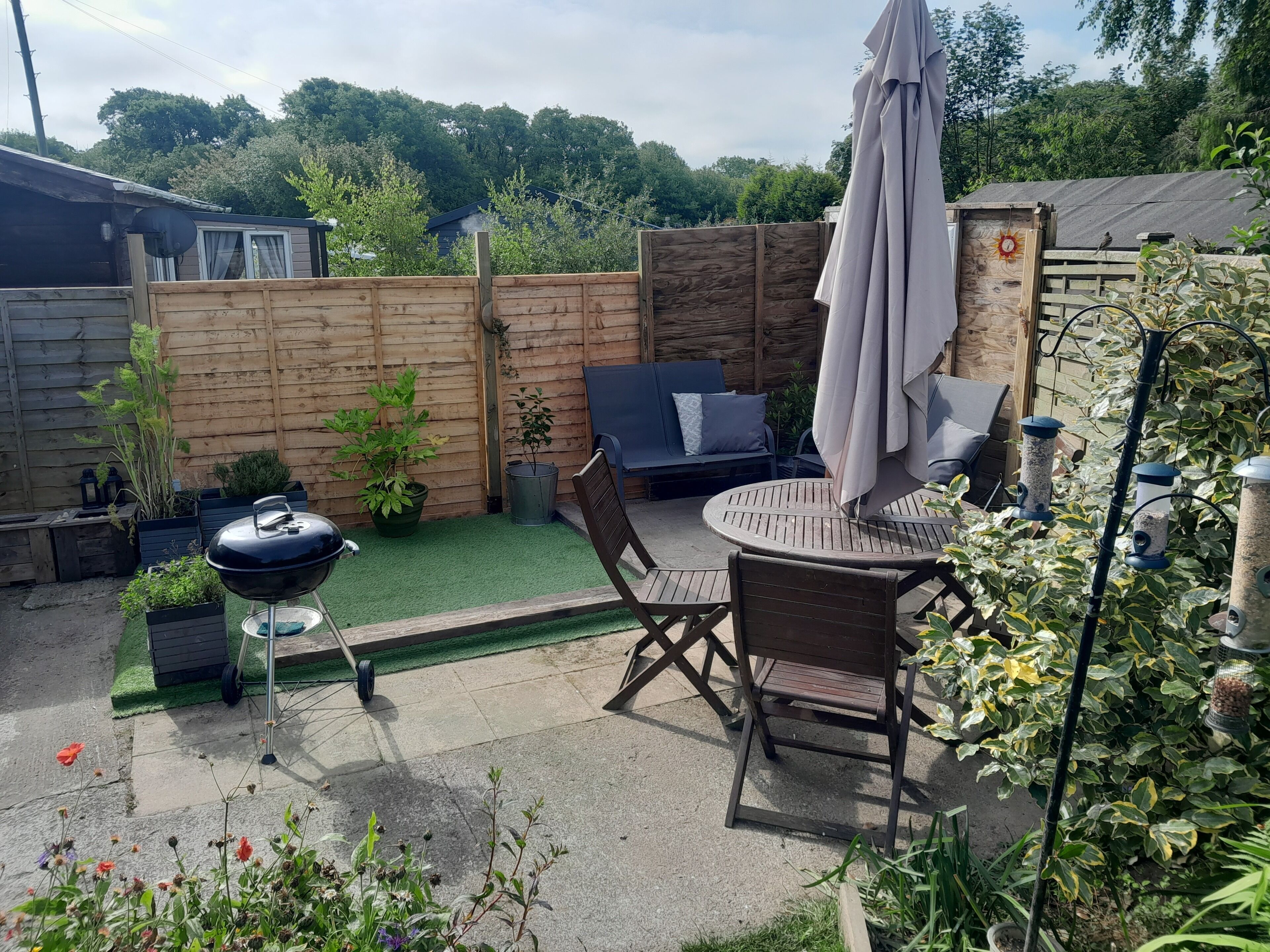 Een achtertuin met een barbecue, een ronde tafel met stoelen, een blauwe bank en een houten omheining.