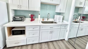 A modern kitchen with white cabinets, a microwave, a coffee maker, and a sink.