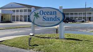 A sign for Ocean Sands, a private community, with a building in the background.