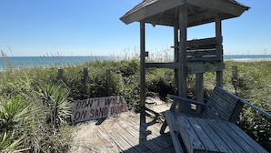 A wooden beach shelter with a sign warning against walking on sand dunes.