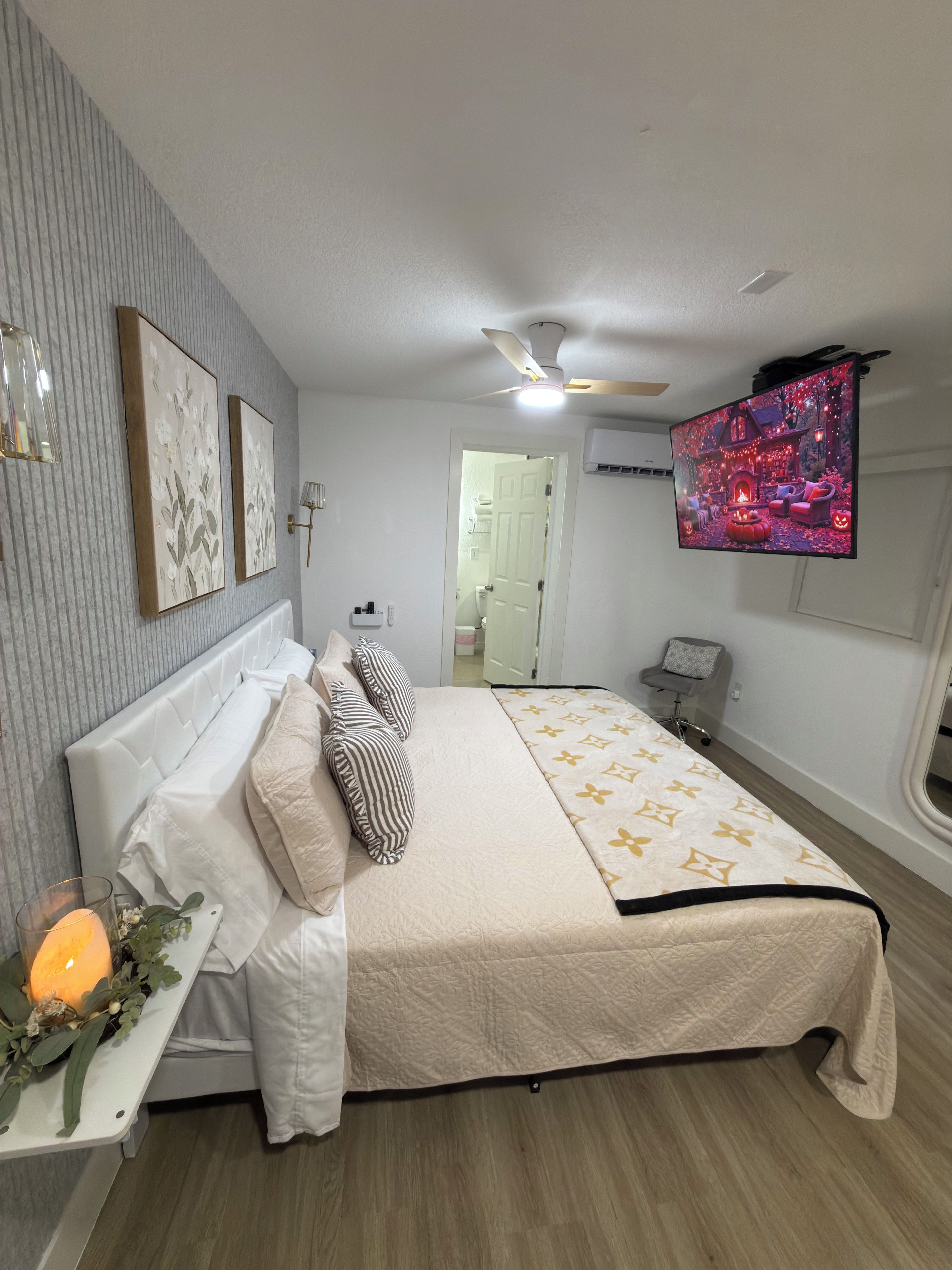 Un dormitorio con cama, mesita de noche, televisor y ventilador de techo.