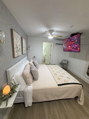 A bedroom with a bed, a bedside table, a TV, and a ceiling fan. - Tampa Skyline (Tampa)
