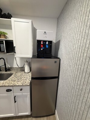 A compact kitchen with a stainless steel refrigerator, a microwave, and a water dispenser.