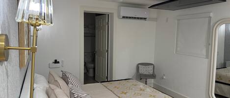 A hotel room with a bed, a standing lamp, a ceiling fan, an air conditioning unit, and a window.