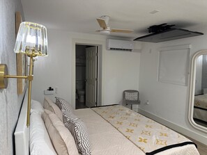 A hotel room with a bed, a standing lamp, a ceiling fan, an air conditioning unit, and a window.