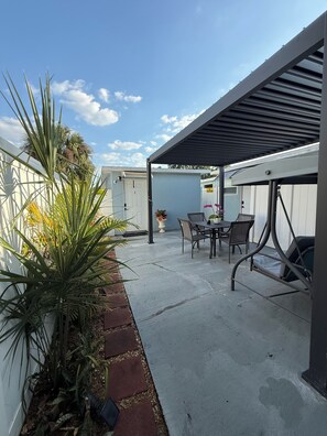 A covered patio area with a table and chairs, surrounded by a concrete floor and a low brick border.