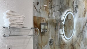 Un baño con inodoro, cabina de ducha de vidrio y salpicadero de mármol.