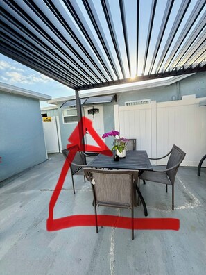 An outdoor patio with a table and chairs, a white fence, and a building in the background. - Tampa Skyline (Tampa)