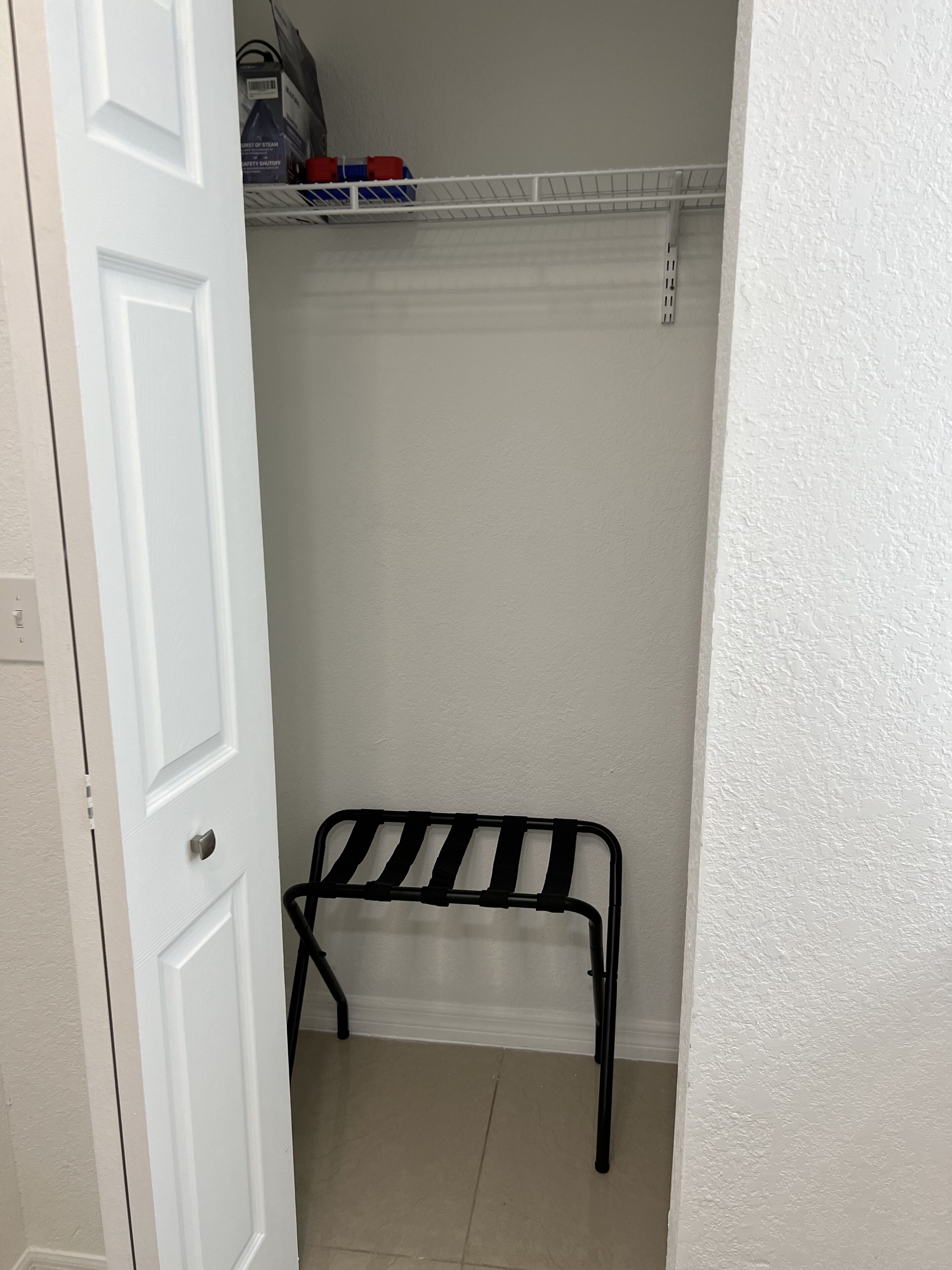 Una puerta blanca que da a un armario con un estante metálico y una silla negra.