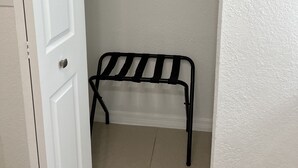 Una puerta blanca que da a un armario con un estante metálico y una silla negra.