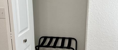 Una puerta blanca que da a un armario con un estante metálico y una silla negra.