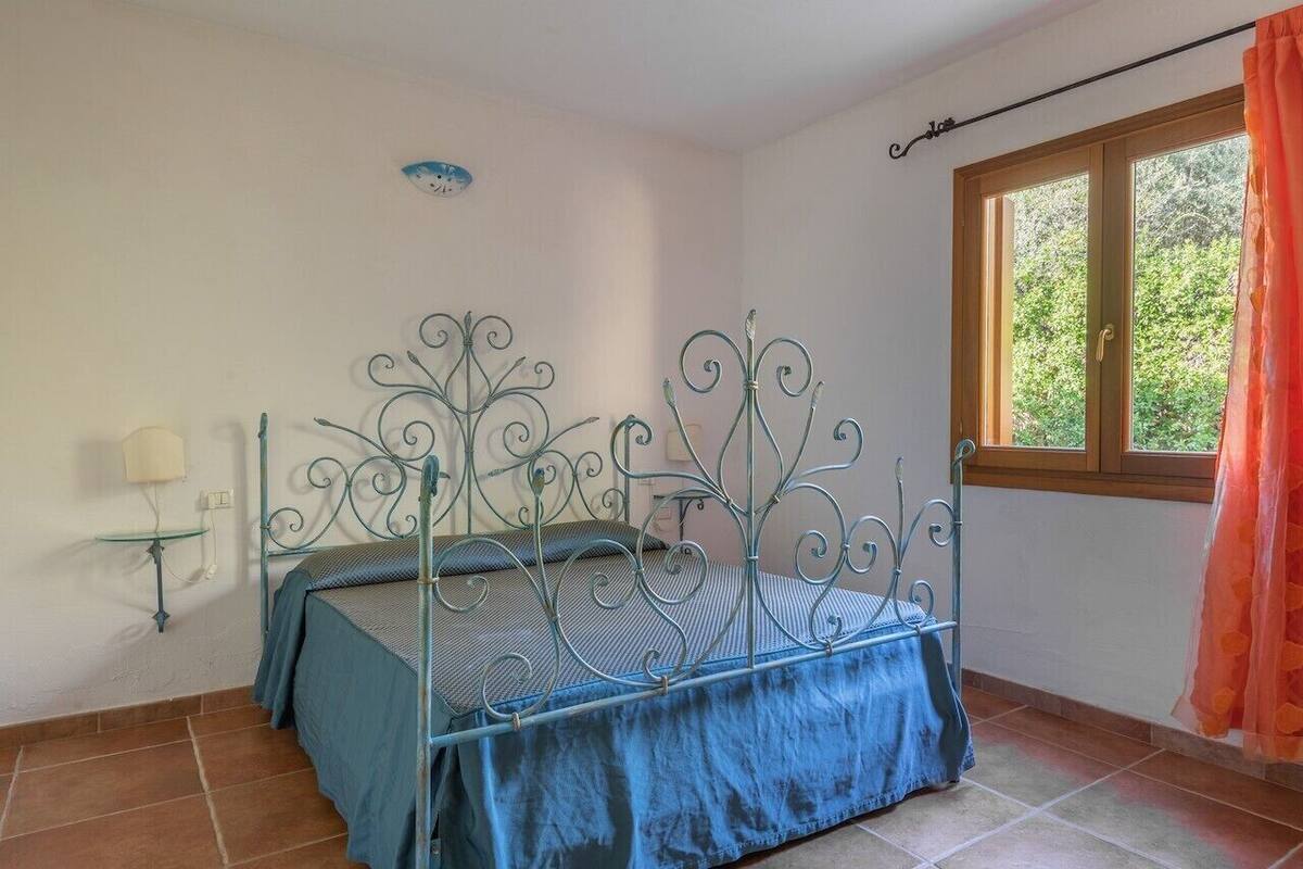 A bedroom with a metal bed frame, a bedside table with a lamp, and a window with curtains.