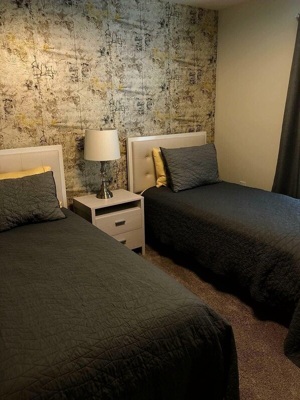 Two single beds with matching bedding and lamps sit beside a textured wallpaper.