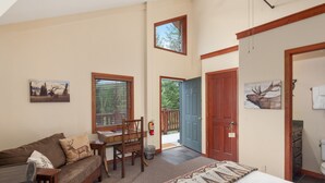 Una habitación acogedora con una cama, un escritorio de madera, una silla, una ventana con persianas, una puerta y un cuadro de un ciervo en la pared.