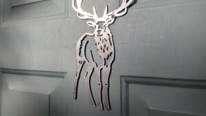 Un trofeo de ciervo metálico montado sobre una pared gris con paneles geométricos.