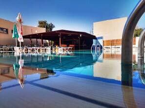 Ein Schwimmbecken mit Liegestühlen und Sonnenschirmen, umgeben von Gebäuden.
